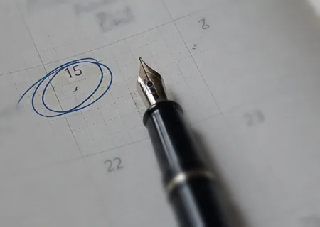 Une date entourée à l'encre bleue sur un agenda de bureau, un stylo plume posé en travers.